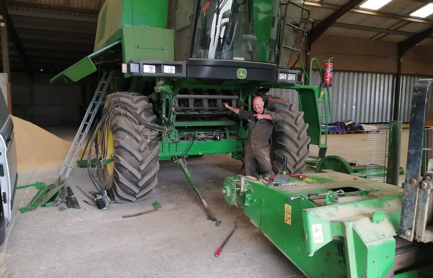 Paul King working underneath a John Deere combine in a shed