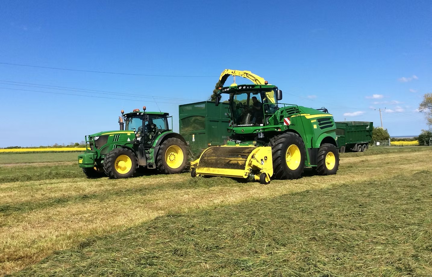 John Deere forage harvester filling a trailer in a grass field